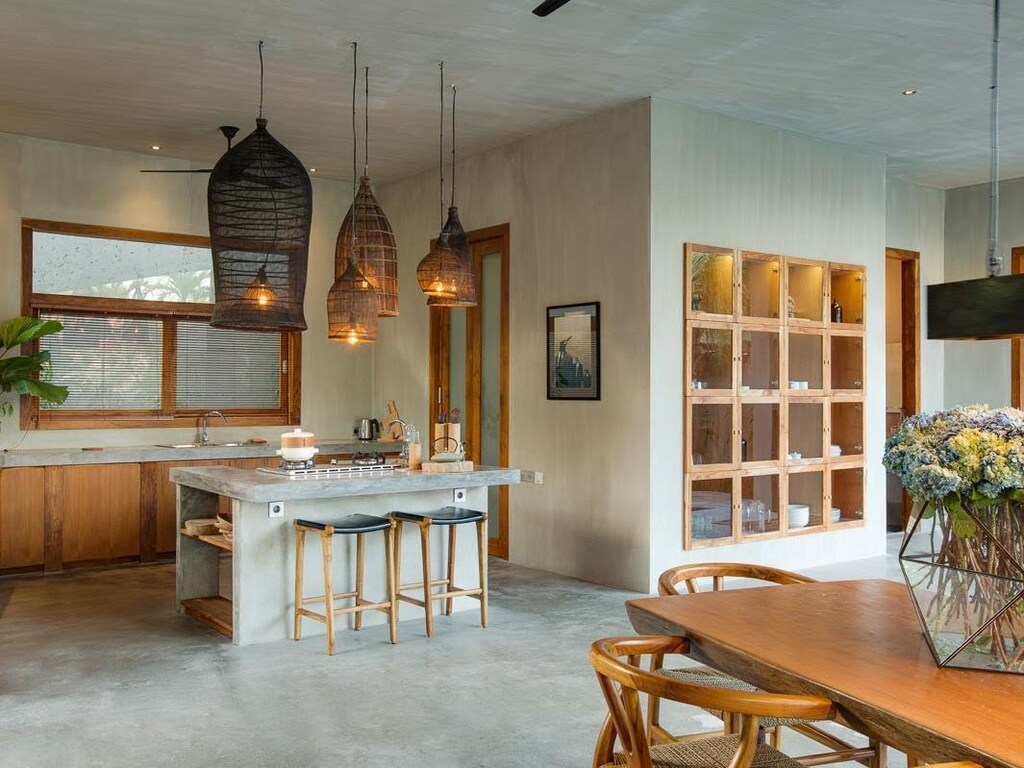 Prachtig interieurontwerp uit Bali, met betonstuc als basis, gecombineerd met mooie warme houten accenten, zoals de inbouw-vitrinekast, houten tafel en barkrukken.