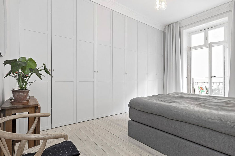 Een grote kast op maat, die de hele muur bezet in deze grote Scandinavische slaapkamer.