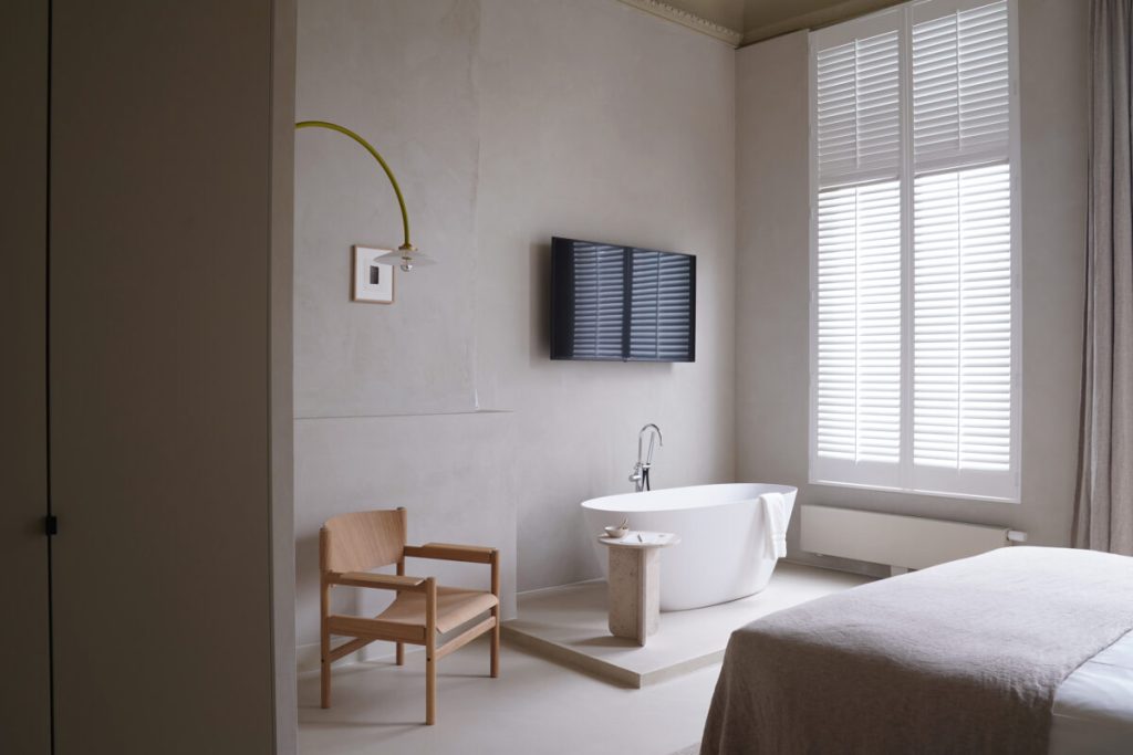 In deze prachtige grote slaapkamer met grote ramen en hoog plafond, is een zithoekje gecreëerd naast een verhoogd podium voor een ovaal vrijstaand bad.