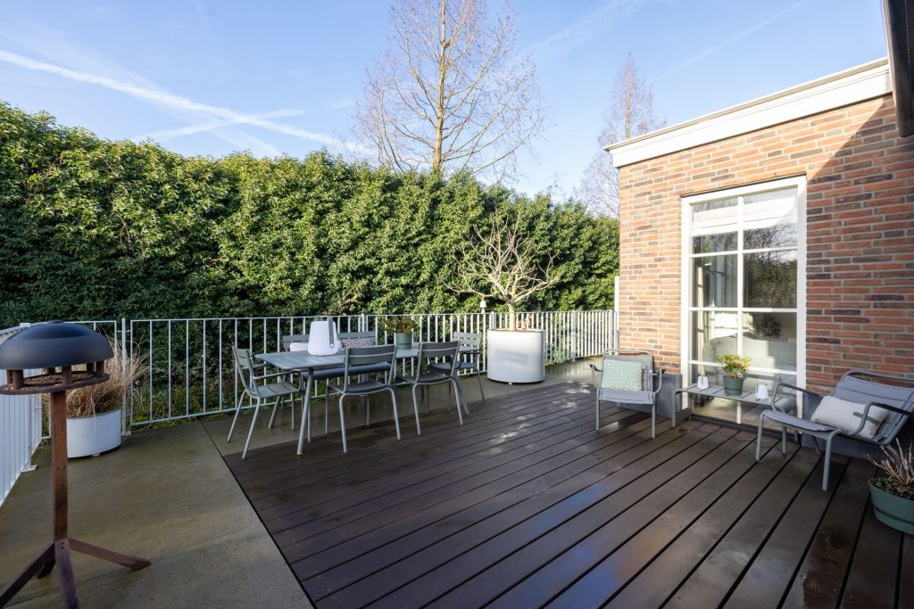Een kleine tuin waar een luxe mix is gebruikt van hardhouten vlonders, grote betonnen tegels, en aluminium meubels.