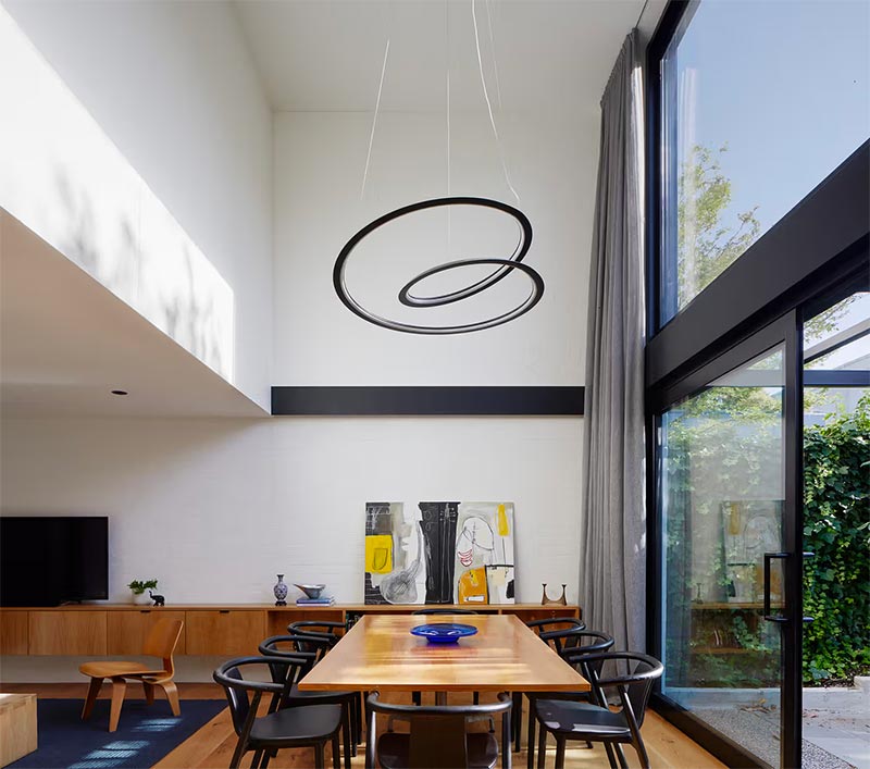 Strakke moderne woon ontworpen door Andrew Child Architect. Aan het hoge plafond is een mooie hanglamp boven de eettafel gehangen. | Fotografie: Tatjana Plitt